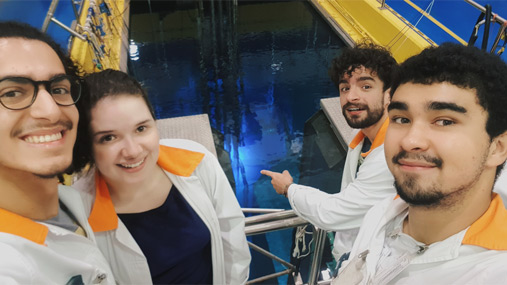 Quatro estudantes do Curso de Ciências Moleculares em uma selfie onde se vê a piscina de um reator no fundo.